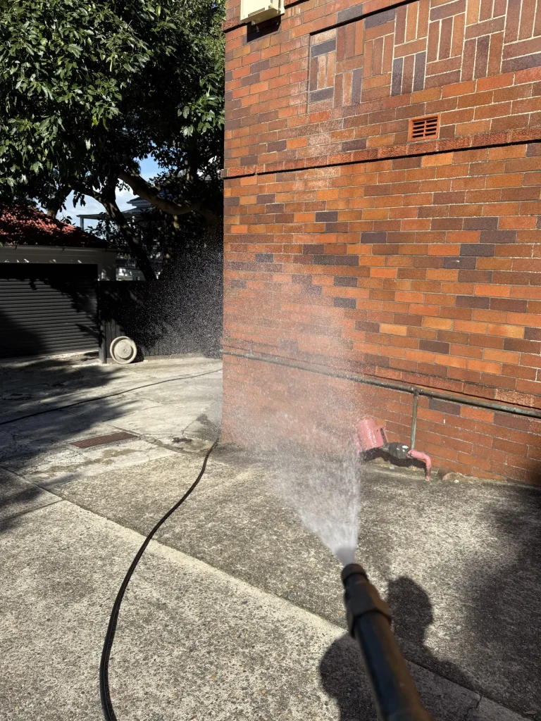 Pest control spray being applied around the exterior wall of a brick house