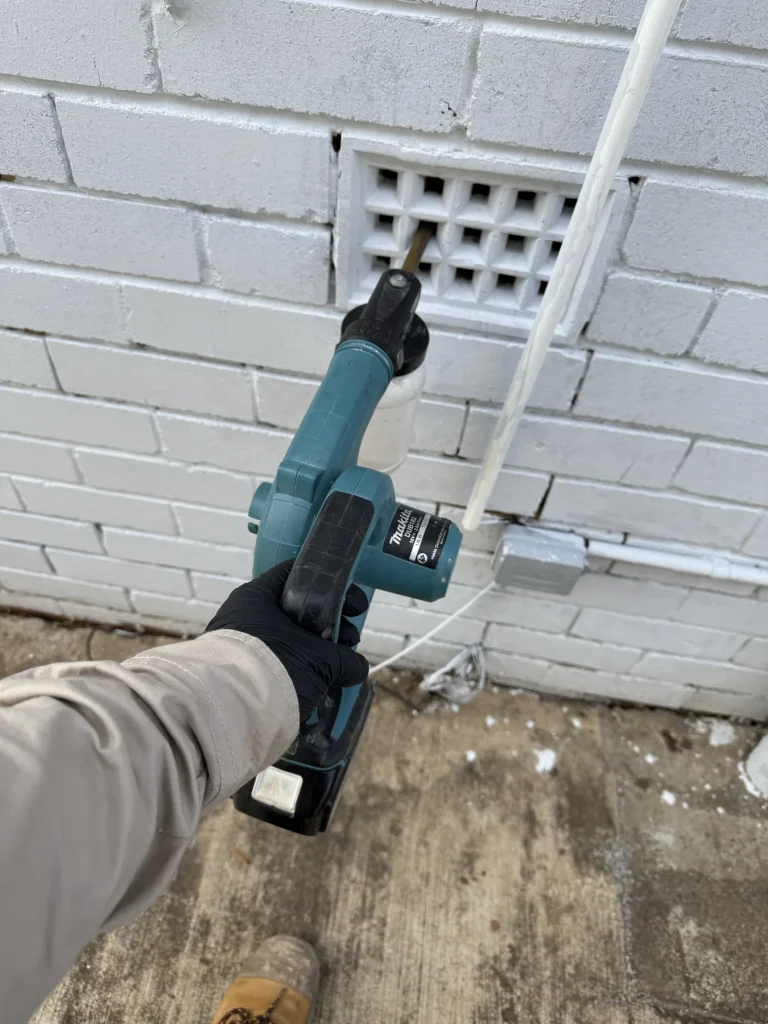 Technician using a drill beside an exterior brick wall vent