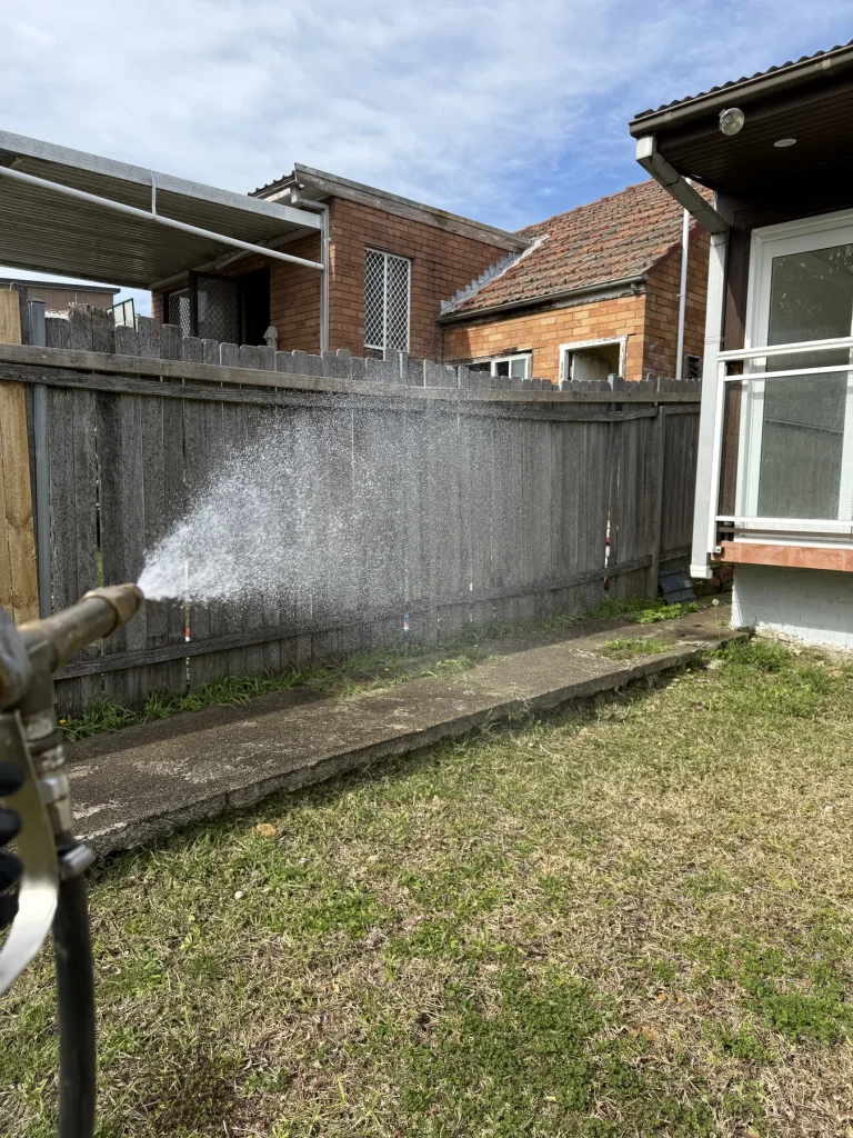 Exterior pest treatment spray along a timber fence and garden edge
