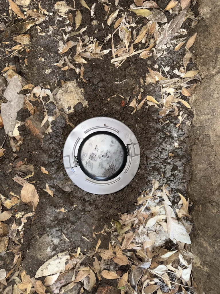 Round pest monitoring station installed in outdoor garden soil