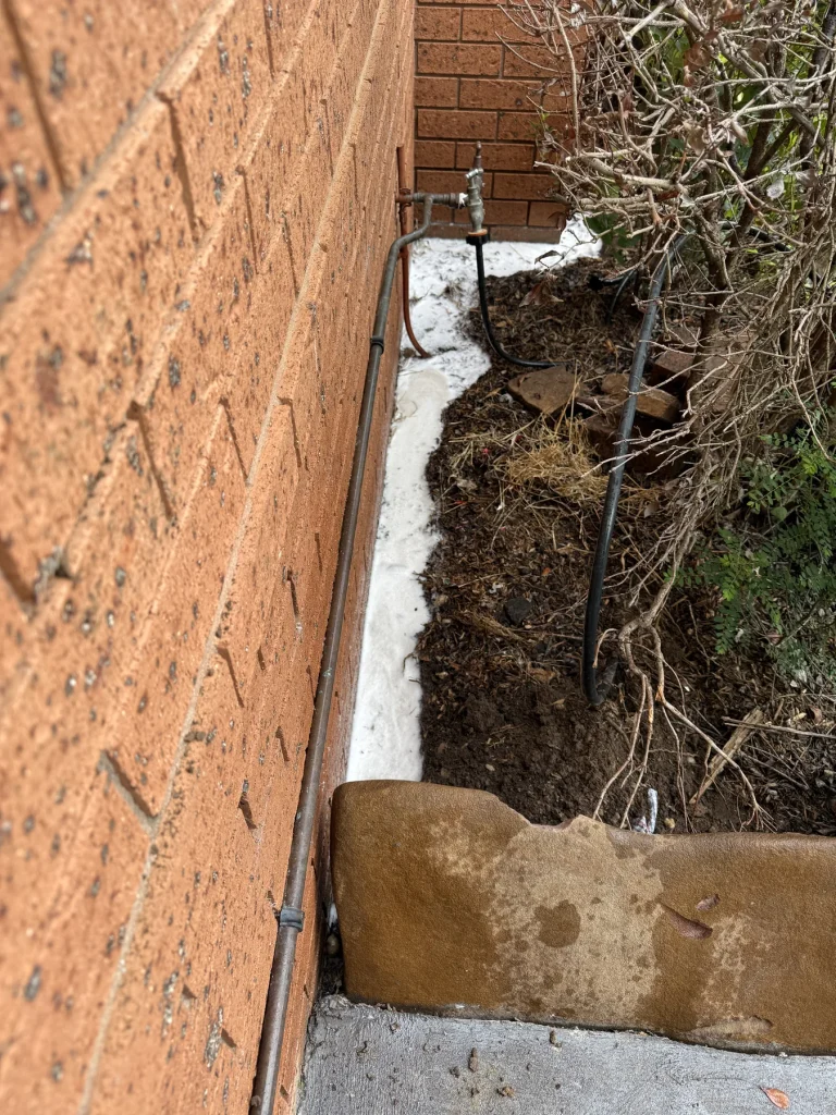 Narrow soil trench excavated alongside an external brick wall