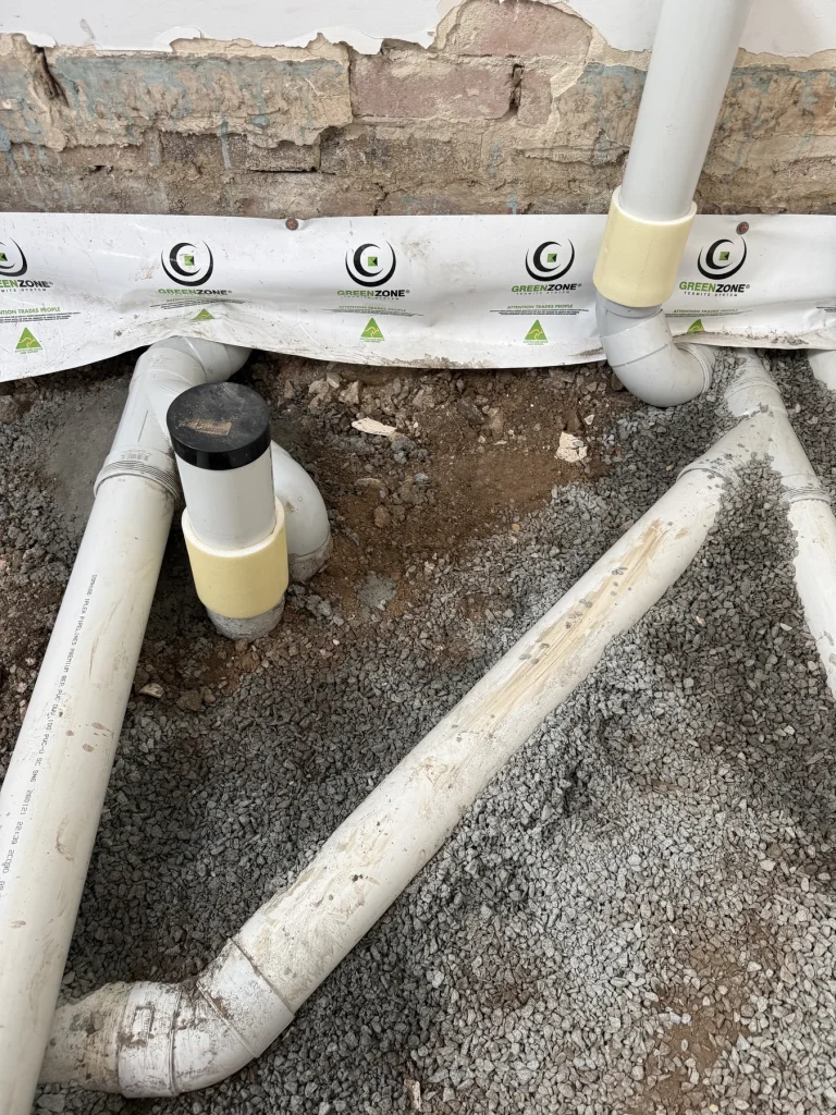White preconstruction termite protection strip beside slab pipework
