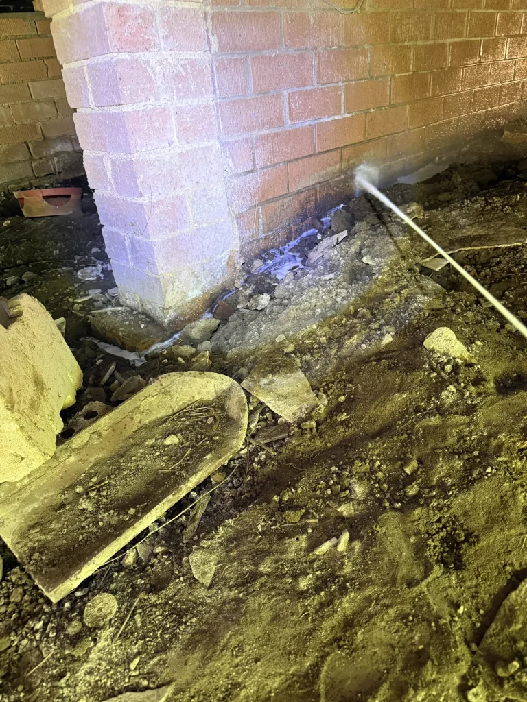 Treatment lance aimed near an interior brick pier in a subfloor