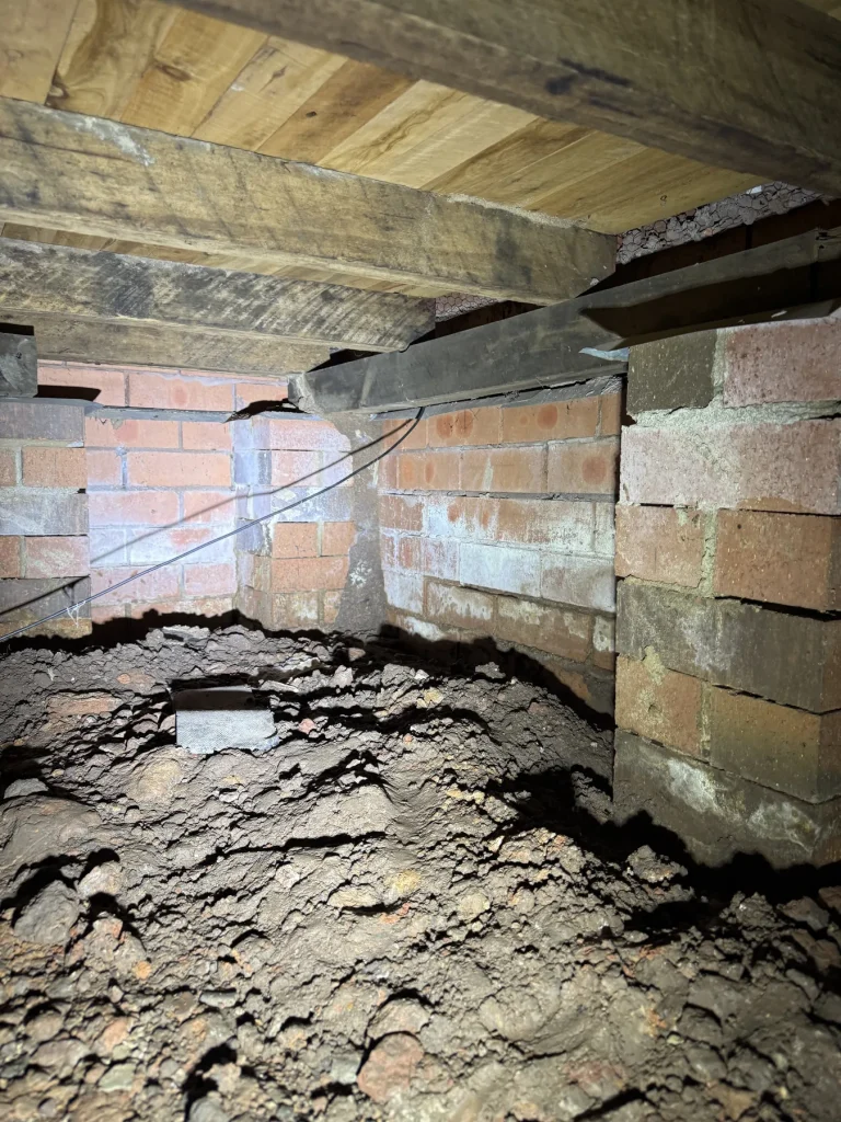 Brick piers and bare soil inside a low residential subfloor