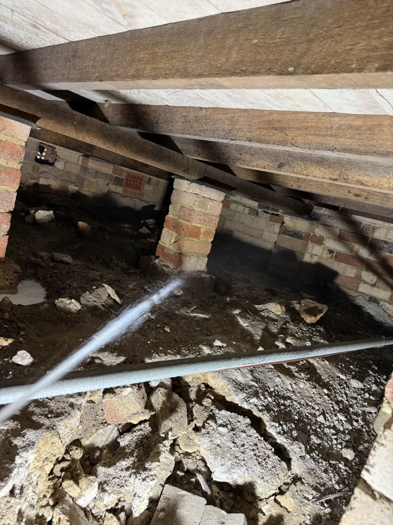 Pest treatment lance directed toward brick foundation inside a subfloor