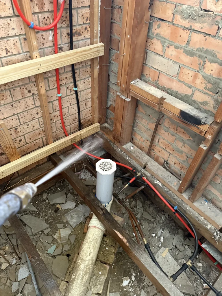 Exposed floor cavity showing framing, pipes and a treatment nozzle